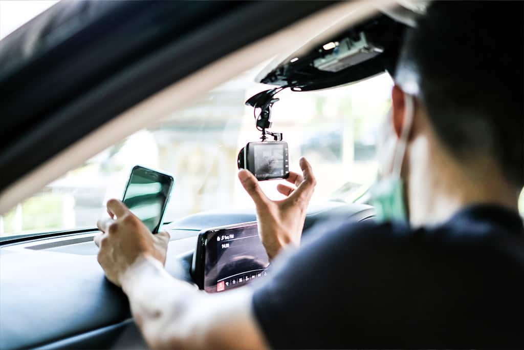 A man positions a dashcam on the passenger side of the windshield