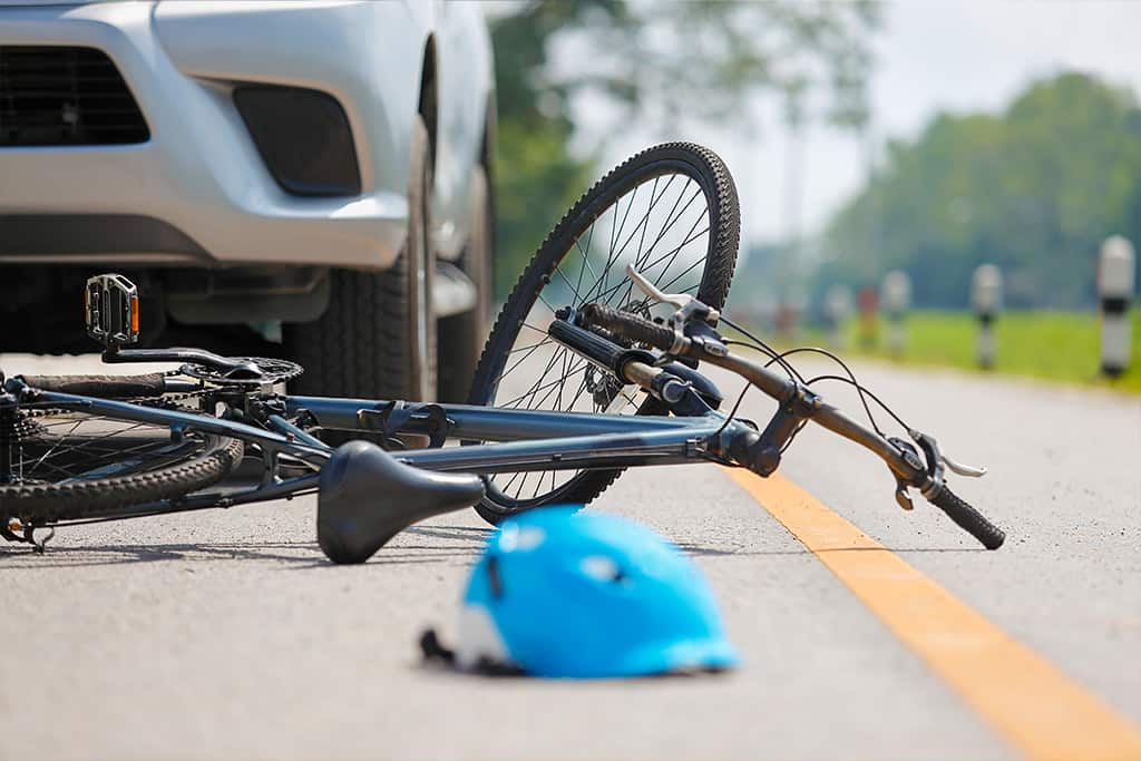 A wrecked bicycle in the foreground with a car in the background