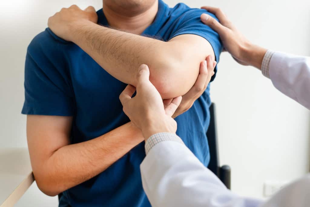 Chiropractor examining from shoulder pain in clinic medical office.