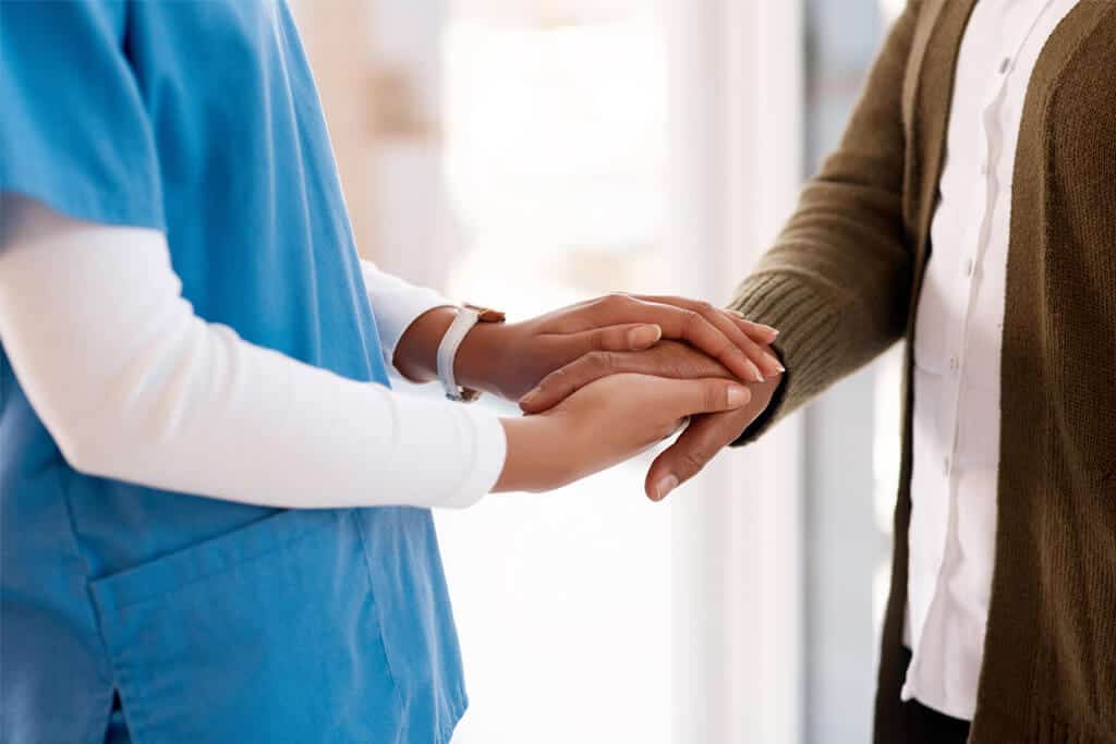 A healthcare worker holding hands with a person for empathy and comforting.