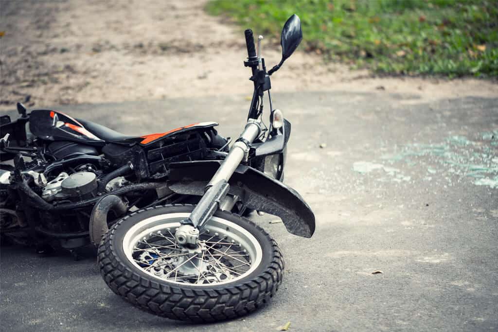 A black motorcycle lying on its side on the road with broken glass scattered around it.