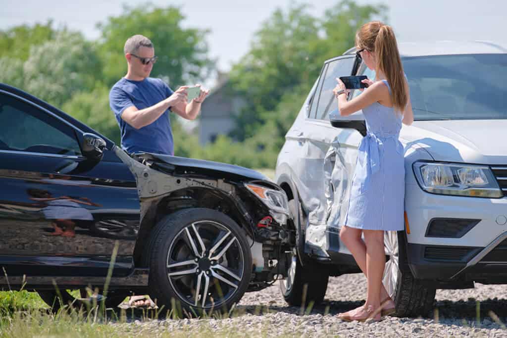Drivers taking pictures on their phones of two vehicles involved in a car accident.