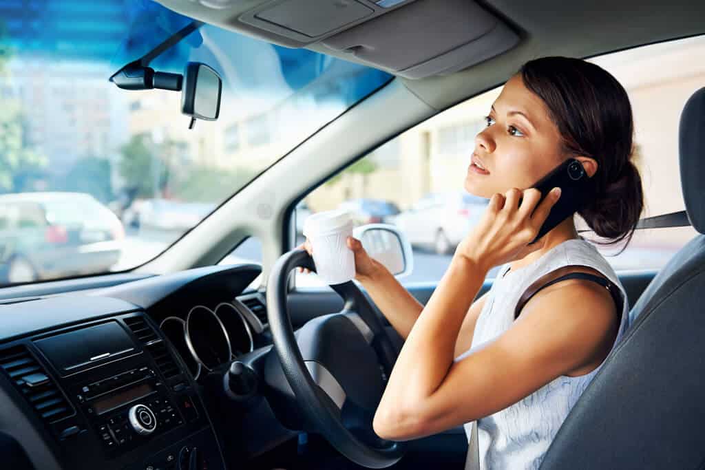 Person multitasking while driving, drinking coffee, and talking on the phone.