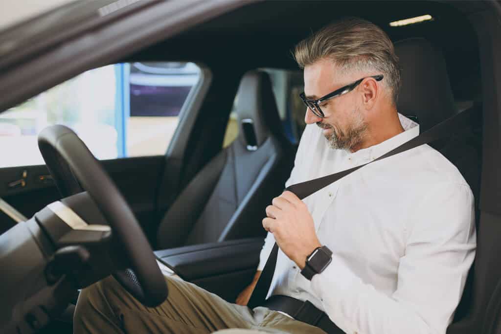 A man in the driver's seat fastening his seat belt.