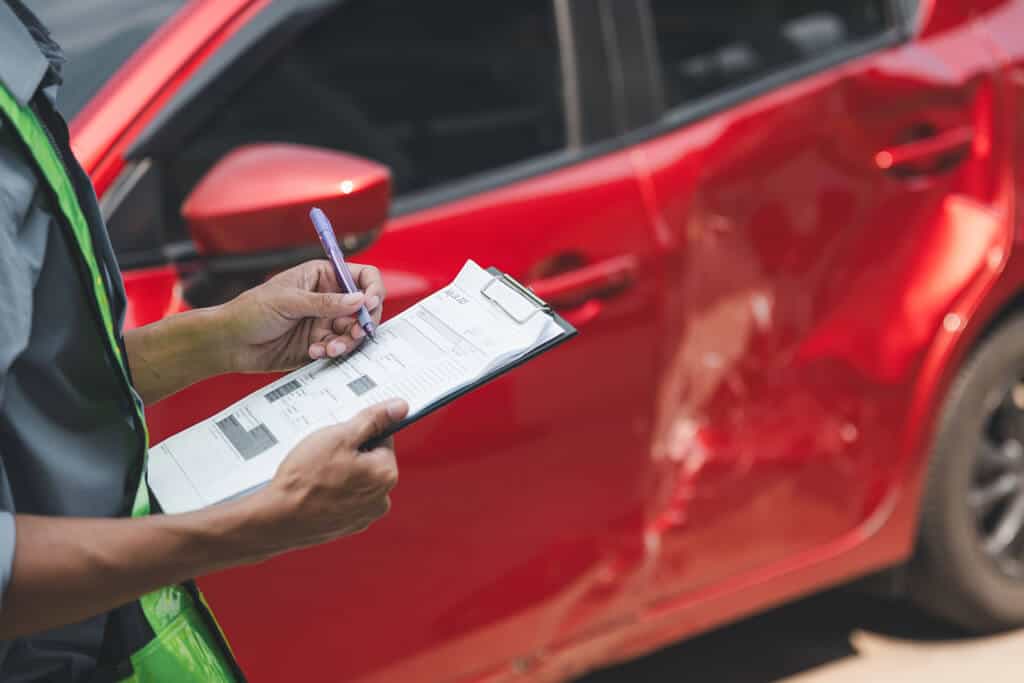 Insurance agent taking nots on a car with a large dent in the door from an accident