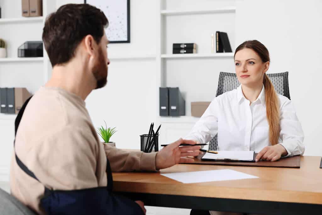 Injured man in a sling is having meeting with a lawyer in an office.