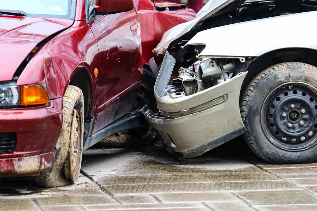 A car accident in the street. A white car crashes into the side of a burgundy car.