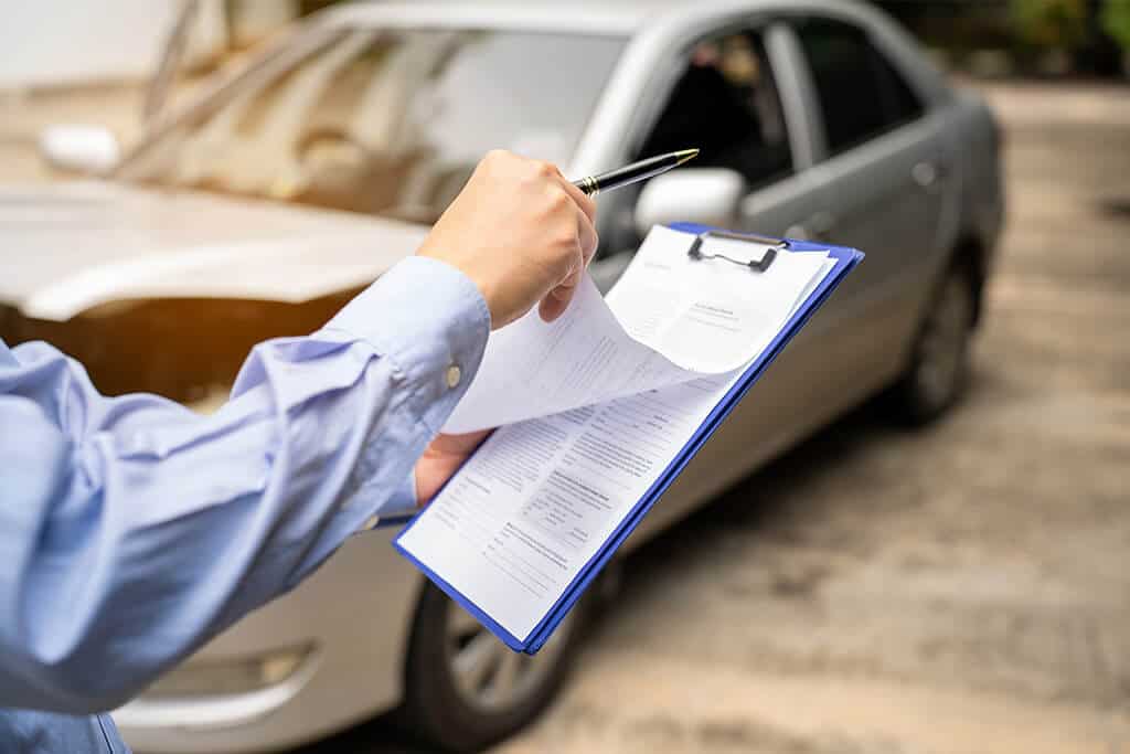 A person writing an insurance claim report on a clipboard after car crash